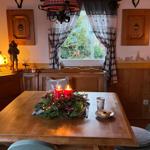 Holztisch mit Kerzen und Weihnachtsdekoration. Fenster mit Gardinen. Holzwände und Decke.