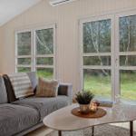 Ein Wohnzimmer mit grauem Sofa, weißem Tisch und großen Fenstern zur Natur.