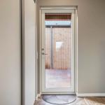 Eingangstür mit Glasfront führt auf eine Holzterrasse mit Holzwand.