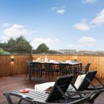 Terrasse mit Tisch, Stühlen und Liegen. Holzgeländer und Blick auf Grünland.
