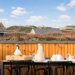 Terrasse mit Tisch und Stühlen, Blick auf Dünenschutz und Häuser im Hintergrund.