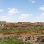 Aus dem Fenster blickt man auf eine Wiese mit Häusern und Dünen im Hintergrund.