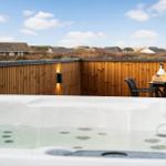 Eine Außenterrasse mit Whirlpool, Holzgeländer und Tisch mit Stühlen.