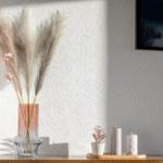On a table are vases with pampas grass, a plant, and candles. A picture hangs on the wall.