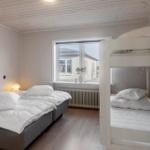 Room with double bed and bunk bed, window, wooden floor, and white walls.