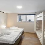 A bedroom with a double bed and a bunk bed. Pictures hang on the wall. Plants sit on the windowsill.