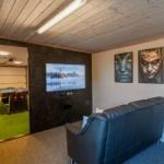 Living room with sofa, TV, and wall art. Passage to room with pool table.