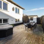 Deck with wood, seating group, and hot tub. Backyard with fence and house.