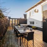 Terrace with long table and chairs, wooden floor, dark wood border, and garden house in background.