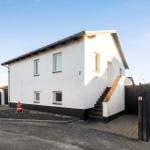 Modern house with white walls and black base, entrance stairs and garden fence.