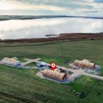 Drei Häuser in Bau auf einer grünen Wiese neben einem See.