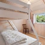 Room with bunk bed, wooden walls, and window with view of greenery.