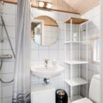 Bathroom with shower, sink, and toilet. White tiles and wooden ceiling.