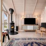 Living room with fireplace, TV, and armchair. Wooden walls and large windows.