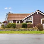 A brown house with a red roof and white door. Garden and street are visible.
