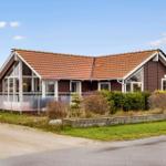 A house with brown cladding and red roof. It has large windows and a terrace.