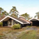 Black wooden house with terrace and garage in forest area.