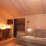 A room with sofa, desk and bed under wooden ceiling.