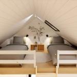 Two beds under sloped ceilings with nightstand and plant.