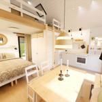 Bedroom with double bed, dining table, and kitchen area under a wooden ceiling.