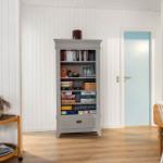 Ein Raum mit Bücherregal, Tisch, Stuhl und Tür. Wände sind weiß verkleidet.