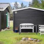 Schwarze Holzhütte mit weißem Gartenmöbel und brennendem Feuerkorb im Gras.