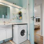 Badezimmer mit Waschmaschine, Spiegelschrank und Glasregalen an hellblauen Wänden.