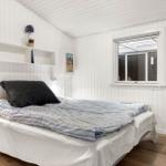 Schlafzimmer mit weiß verkleideten Wänden, Bett mit blau gemustertem Bettzeug und Fenster.