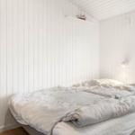 Schlafzimmer mit Bett, Fenster und Holzwand. An der Wand hängt eine Lampe.