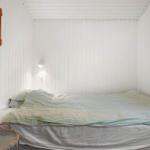Schlafzimmer mit Bett, Wandlampe und Holzregal an der Wand.