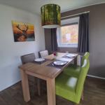 Essbereich mit Tisch, Stühlen und Wandbild. Fenster mit Vorhängen.