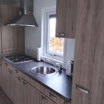 Küche mit Holzschränken, Herd, Spüle und Fenster.