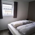 Schlafzimmer mit Doppelbett, Fenster und Vorhängen.