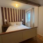 Schlafzimmer mit Bett, Nachttischen und Streifenwand. Holzbalken an der Decke.