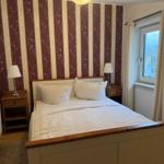 Schlafzimmer mit Doppelbett, gestreifter Tapete und Fenster mit Vorhängen.