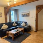 Wohnzimmer mit L-förmigem Sofa, Holzfußboden und Holzrahmen. Tisch und Teppich sind vorhanden.