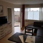 Wohnzimmer mit Sofa, TV und Terrasse. Fenster mit Jalousien.