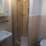 Bad mit Dusche, Waschbecken und Toilette. Fliesenwand und Spiegel.