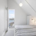 Bedroom with balcony, white furnishings, and sloped ceiling.