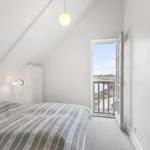 Bedroom with balcony view, white walls, and simple furnishings.