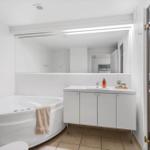 Bath with whirlpool, sink, and mirror. Entrance to sauna.