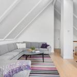 Living room with gray sofa, striped rug, and sloped ceiling beams.