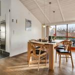 Dining area with wooden table and chairs, view of garden. Kitchen area with refrigerator.