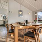 Dining room with wooden table, chairs, and garden view. Kitchen in the background.
