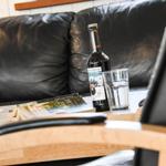 On the table is a bottle of beer and a glass next to a book and a chair.