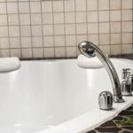 A bathtub with showerhead and faucets, surrounded by tiles and stone tiles.