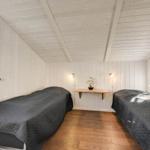 Two beds with dark covers, wooden floor, and white paneled walls with ceiling structure.