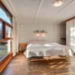 Bedroom with wooden floor, large window, and white bed. A shelf with two lamps hangs on the wall.