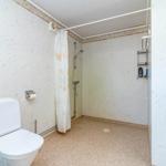 Bad mit Dusche, Toilette und Regal an der Wand.
