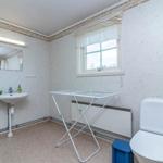 Badezimmer mit Waschbecken, Toilette und Wäscheständer. Fenster mit Vorhang. Wandverkleidung und Bodenfliesen.